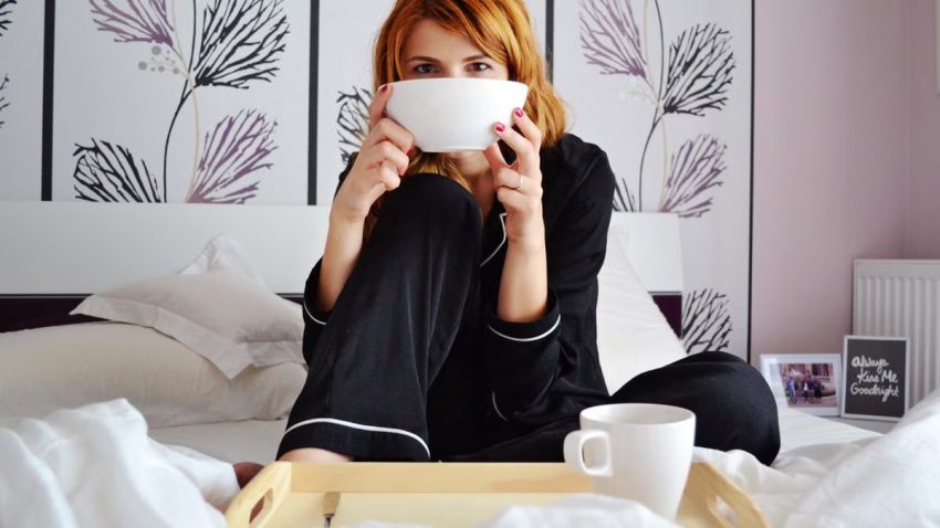 A woman enjoys a cup of coffee in a stylish and cozy bedroom, perfect for relaxation.